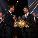 Two men in suits holding a championship belt on a stage with applause in the background