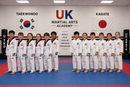 Group of children in martial arts uniforms posing in a classroom with UK Martial Arts Academy branding.