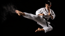Person in a white martial arts uniform performing a high kick against a black background