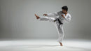 Person in a white martial arts uniform performing a high kick on a plain background