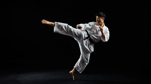 Person in a white martial arts uniform performing a high kick against a black background